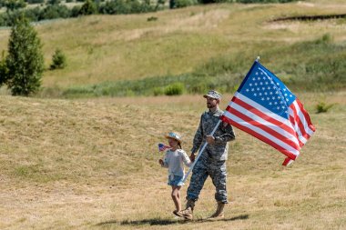 askeri adam ve mutlu vatansever çocuk yürüyüş ve Amerikan bayrakları tutan 