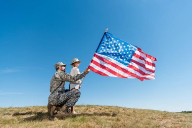 askeri üniformalı baba ve gökyüzüne karşı Amerikan bayrağı tutan çocuk 
