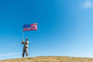 yıldız ve çizgili Amerikan bayrağı ile yürüyüş üniformalı yakışıklı askeri adamın düşük açı görünümü 
