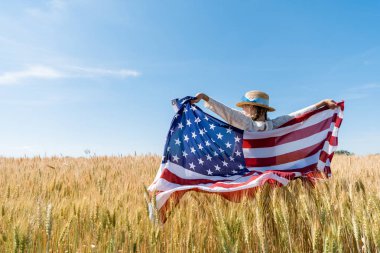 altın alanda Amerikan bayrağı tutan hasır şapkalı çocuğun arka görünümü 