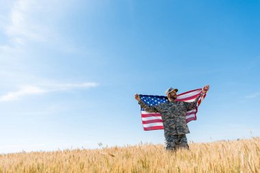 soldier in cap and military uniform holding american flag in field  clipart
