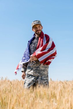 şapkalı ve üniformalı mutlu askerin seçici odak alanında Amerikan bayrağı tutan 