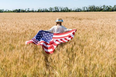 altın alanda yıldız ve çizgili amerikan bayrağı tutan hasır şapka lı çocuğun arka görünümü 