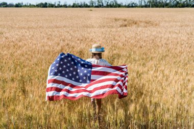 altın alanda yıldız ve çizgili amerikan bayrağı tutan hasır şapkalı çocuğun arka görünümü 