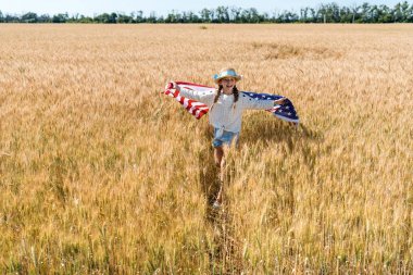 cute and happy child holding american flag with stars and stripes in golden field  clipart