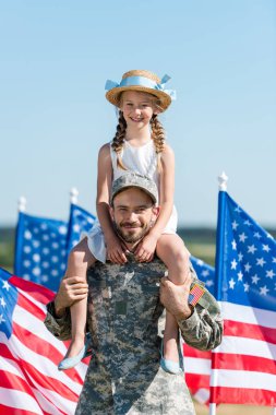 amerikan bayrakları yakınında hasır şapkalı sevimli kızı omuzlarında tutan yakışıklı adam 