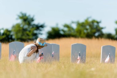 mezarlıkta Amerikan bayrağı ile mezar taşı yakınında oturan sevimli çocuk 