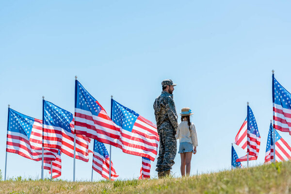 man in military uniform standing with daughter near american flags 