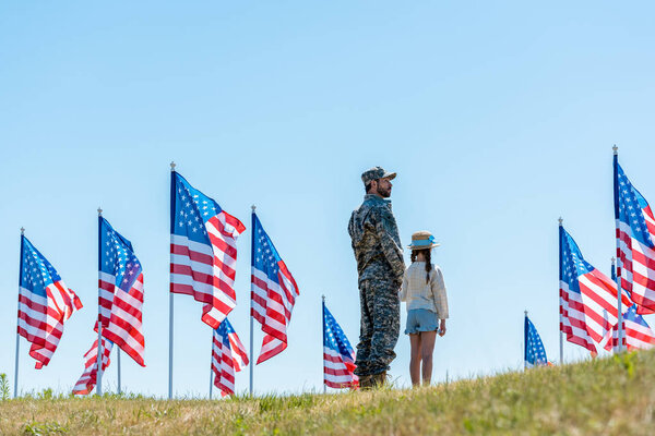 military man in uniform standing with daughter near american flags 