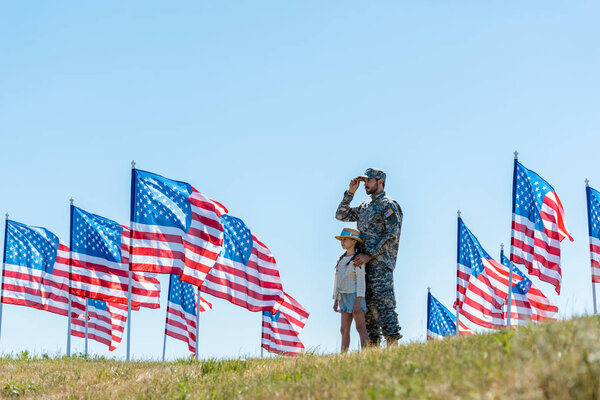 selective focus of father in military uniform standing with cute kid near american flags 