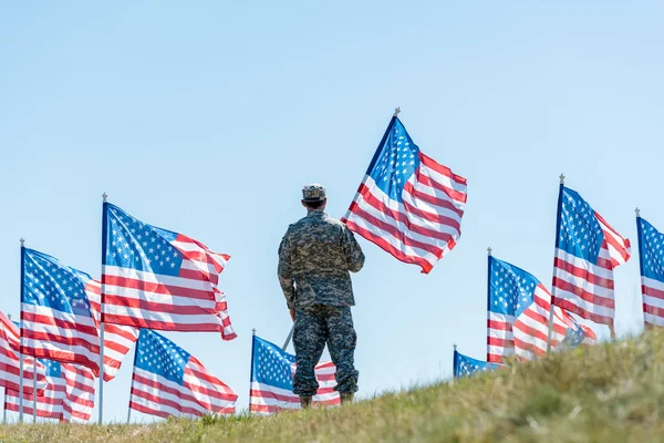 Tyłu Widok Żołnierza Mundurze Wojskowym Cap Stoi Trzyma Amerykańską Flagę — Zdjęcie stockowe