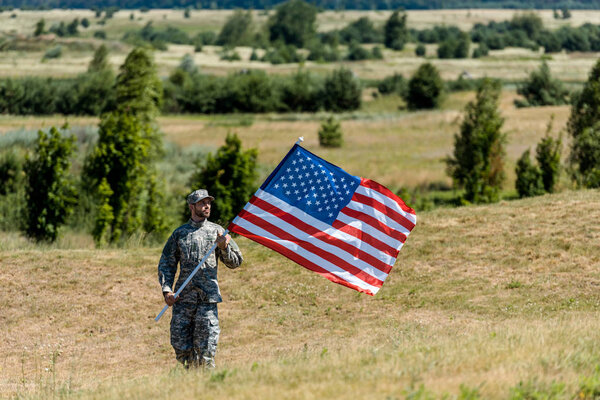 selective focus of military man in uniform and cap holding american flag in summertime 