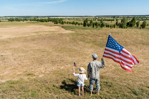 Achteraanzicht Van Militaire Vader Patriottische Kid Holding Amerikaanse Vlaggen — Stockfoto