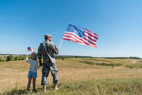 солдат, держащийся за руки с ребенком и держащий американский флаг
 