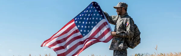 Panoramautgave Kjekk Militær Mann Med Ryggsekk Som Holder Amerikansk Flagg – stockfoto