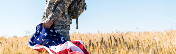 панорамный снимок патриотического солдата в военной форме, держащего американский флаг на поле боя
 