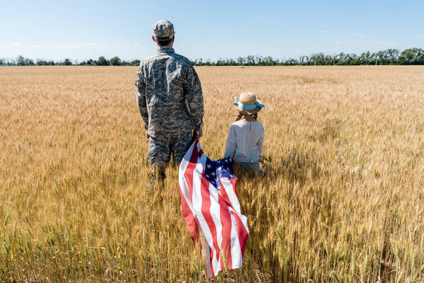 back view of soldier and child standing in field and holding american flag 