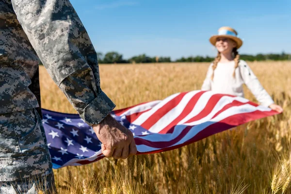 フィールドで娘とアメリカの旗を保持する軍服を着た男のトリミングされたビュー — ストック写真