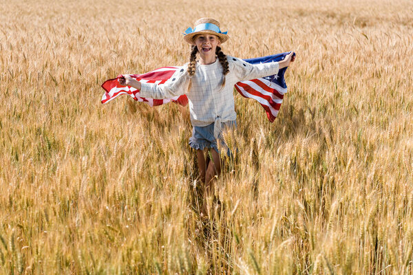 happy kid in straw hat holding american flag in golden field 