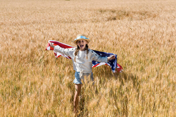 cute and happy kid holding american flag in golden field 