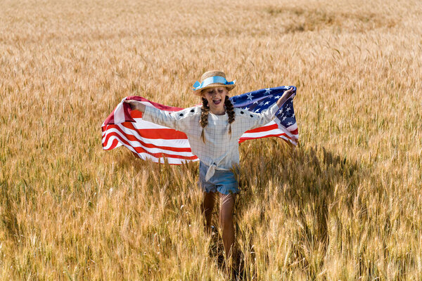 cute and happy child holding american flag in golden field 