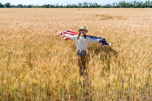 cute and cheerful kid holding american flag with stars and stripes in golden field 