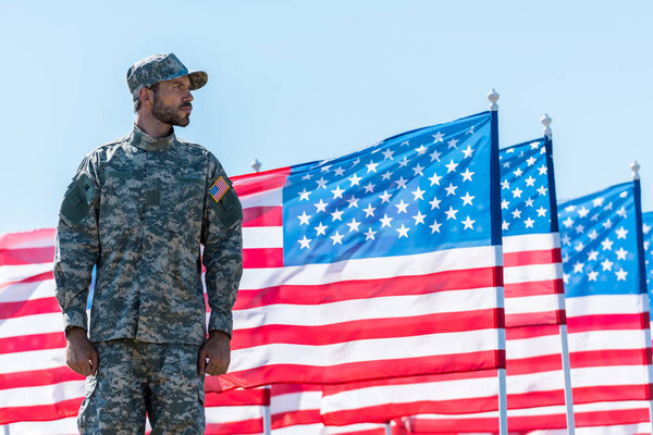 soldier in uniform standing near american flags against blue sky 