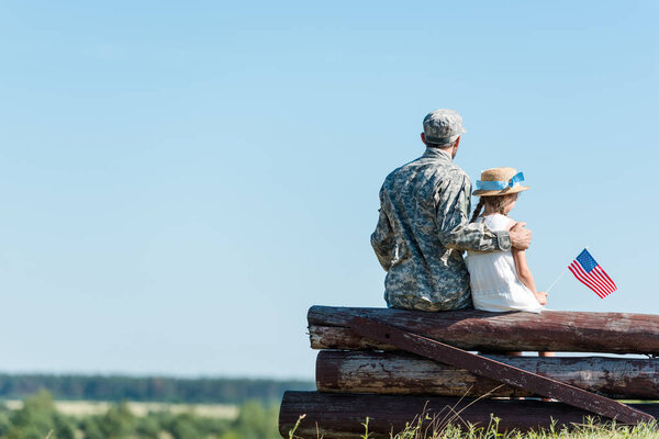 Ребенок-патриот держит российский флаг рядом с отцом-ветераном, сидя в заборе
 