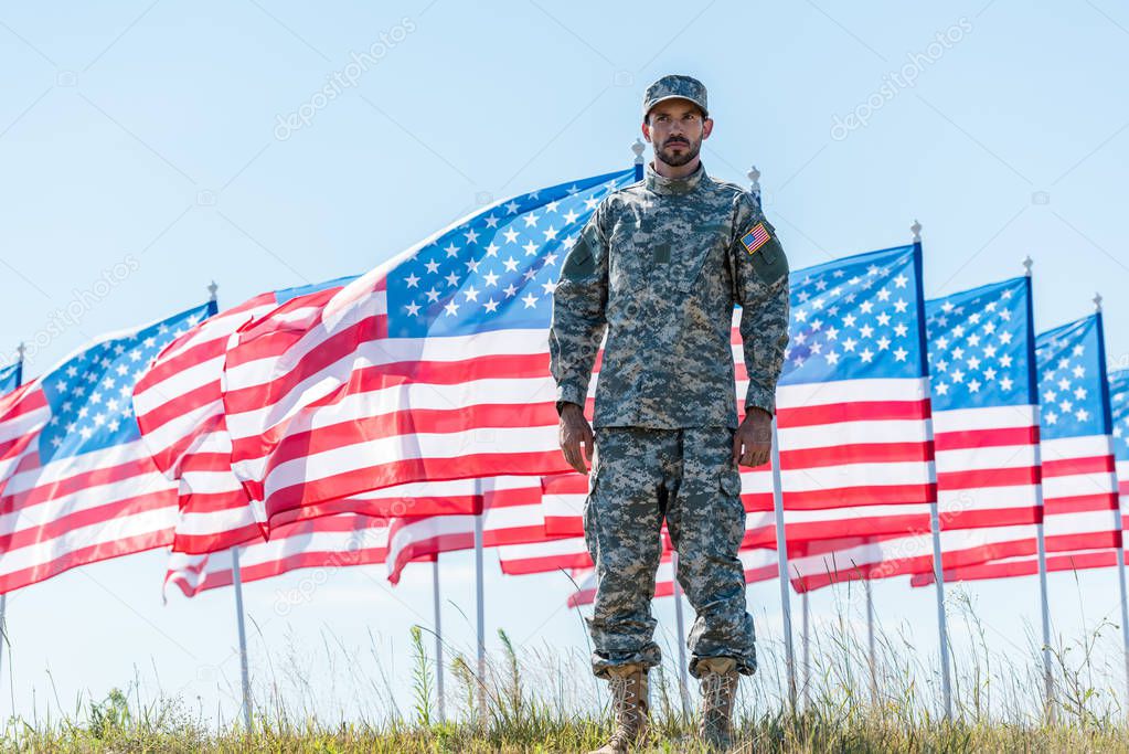 handsome soldier in uniform standing near american flags and blue sky 