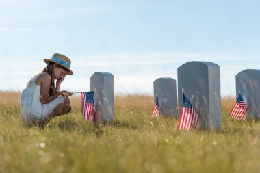 Amerikan bayrakları ile mezar taşları yanında otururken çocuk kaplama yüzü seçici odak 