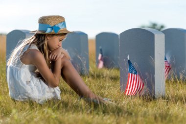 üzgün çocuk oturma ve Amerikan bayrakları ile mezar taşları bakarak seçici odak 