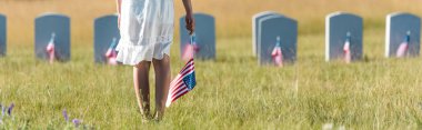 panoramic shot of child in white dress standing on graveyard with american flag  clipart