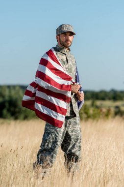 kamuflaj üniformalı askeri adam ve altın alanda Amerikan bayrağı tutan şapka 