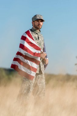 kamuflaj üniformalı ve altın alanda Amerikan bayrağı tutan şapkalı adamın seçici odak 
