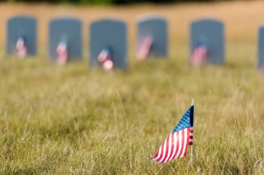 selective focus of american flag with stars and stripes near gravestones  clipart
