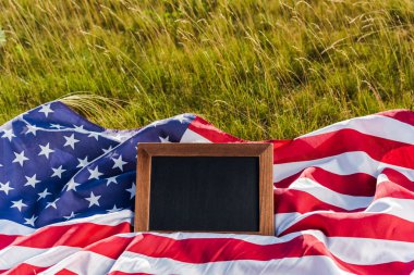 blank chalkboard on american flag with stars and stripes on green grass clipart