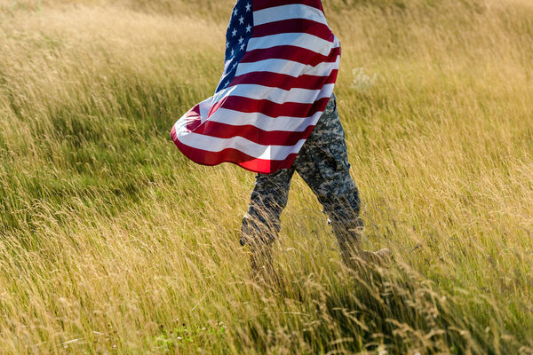 cropped view of man in camouflage uniform holding american flag in field 