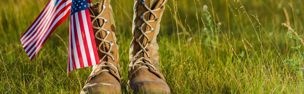 panoramic shot of military boots near american flag with stars and stripes on grass 