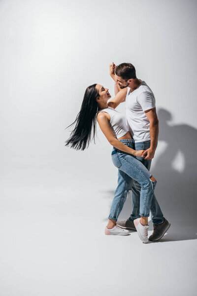 Вид в полный рост молодой пары, обнимающейся, держащейся за руки и смотрящей друг на друга
