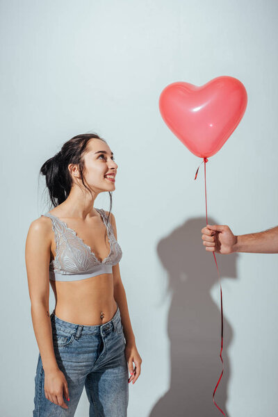 cropped view of man giving red balloon in heart form to attractive girl