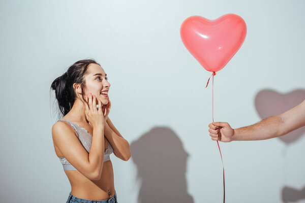 cropped view of man giving red balloon in heart form to attractive happy girl