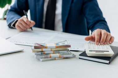 cropped view of businessman using calculator near money and contract 