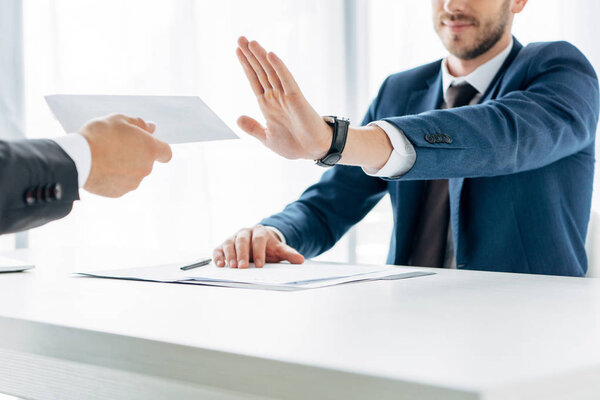 cropped view of man gesturing near business partner giving envelope with bribe in office 