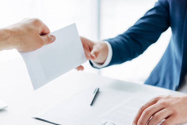 обрезанный вид человека, дающего конверт с взяткой деловому партнеру за столом
 