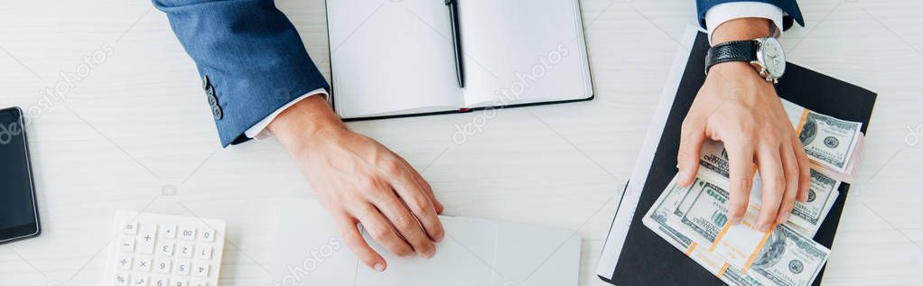 top view of man touching bribe while sitting near notebook and laptop 