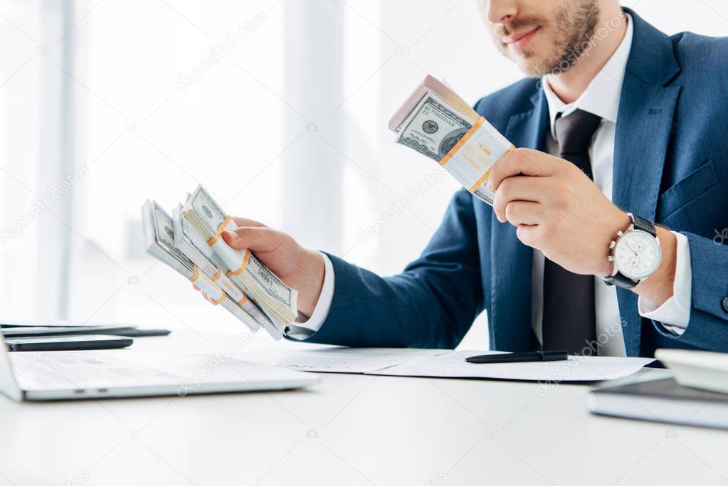 cropped view of businessman in suit holding bribe in office 