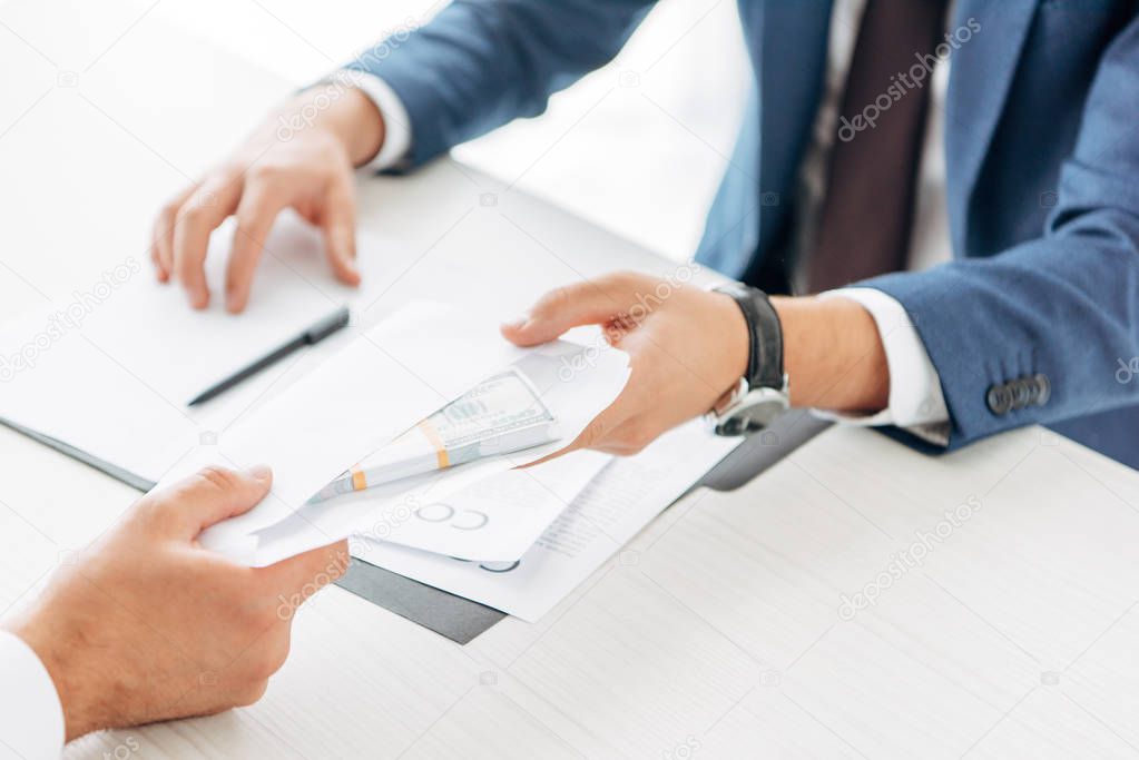 cropped view of businessman giving envelope with money to business partner 