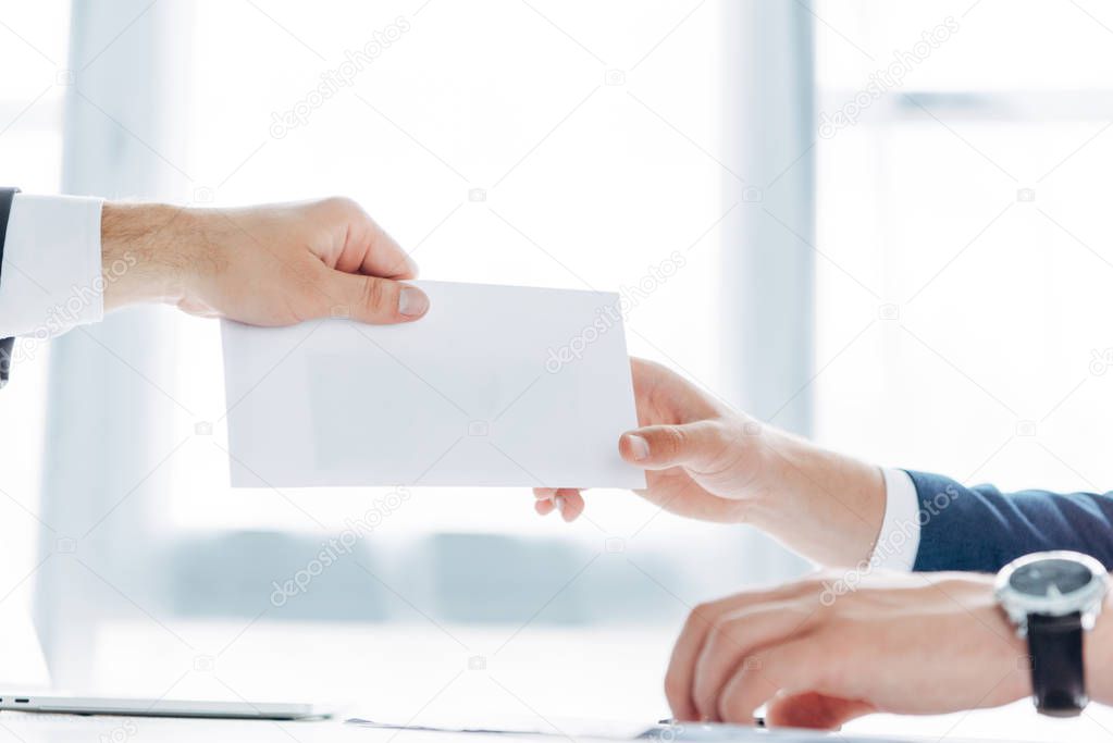 cropped view of businessman giving white envelope with bribe to business partner 
