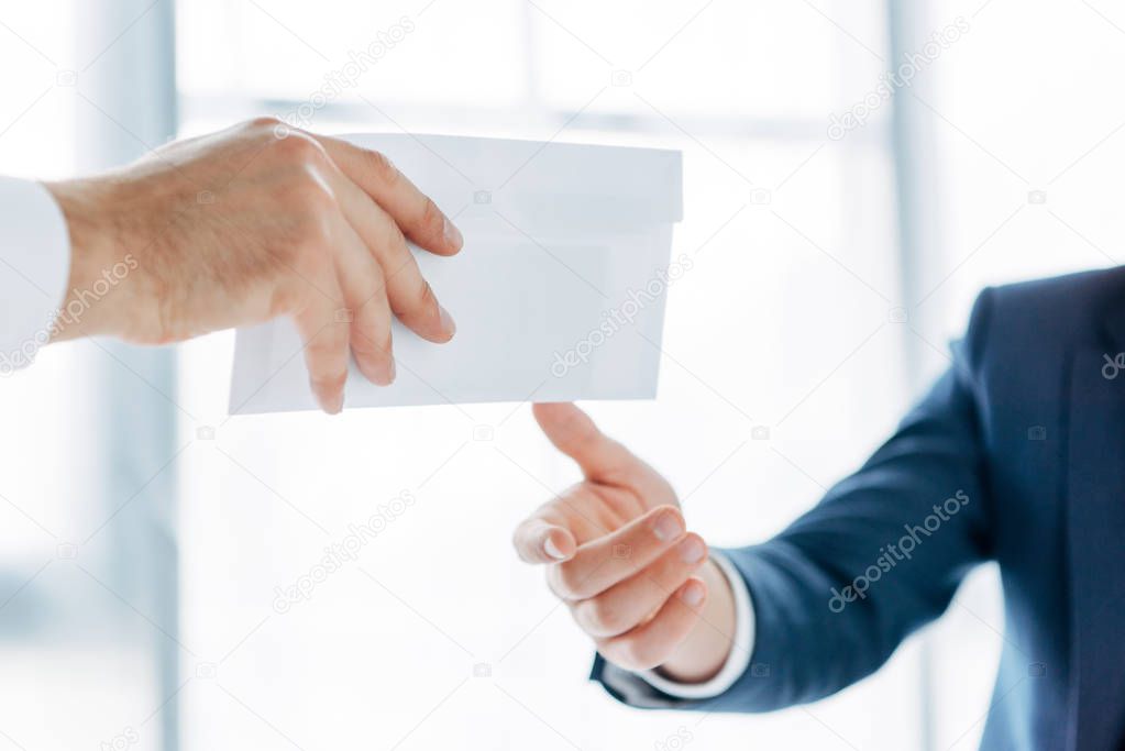 cropped view of businessman giving white envelope with bribe to business partner in office 