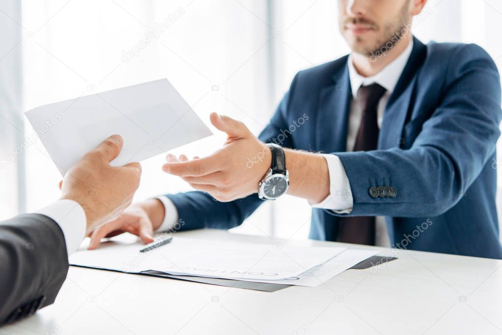 cropped view of man giving envelope with bribe to business partner near table 